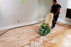 A man uses a large sander to sand the floors in an older home that is being renovated.